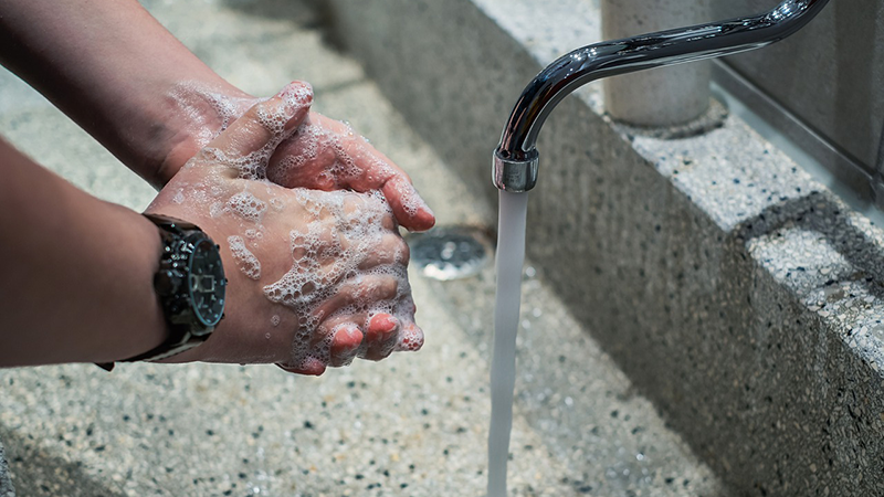 hands rubbing soap together along with a turned on water faucet