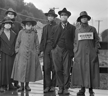 People in quarantine masks, one with a sign that says wear a mask or go to jail