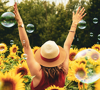 Lady in straw hat, with hands raised, in a field of sunflowers