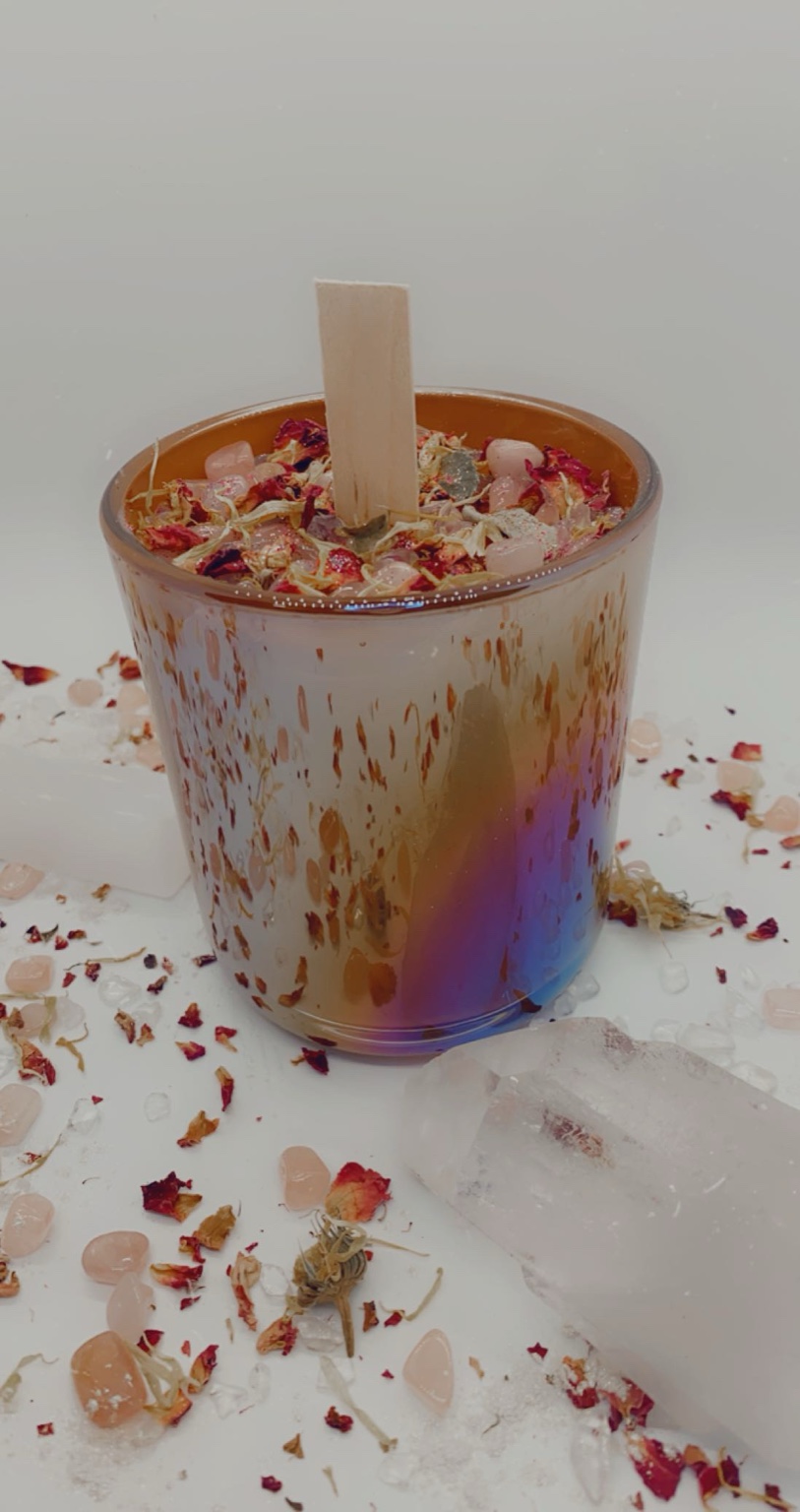 Handcrafted intention candle in an iridescent vessel surrounded by botanicals and crystals.