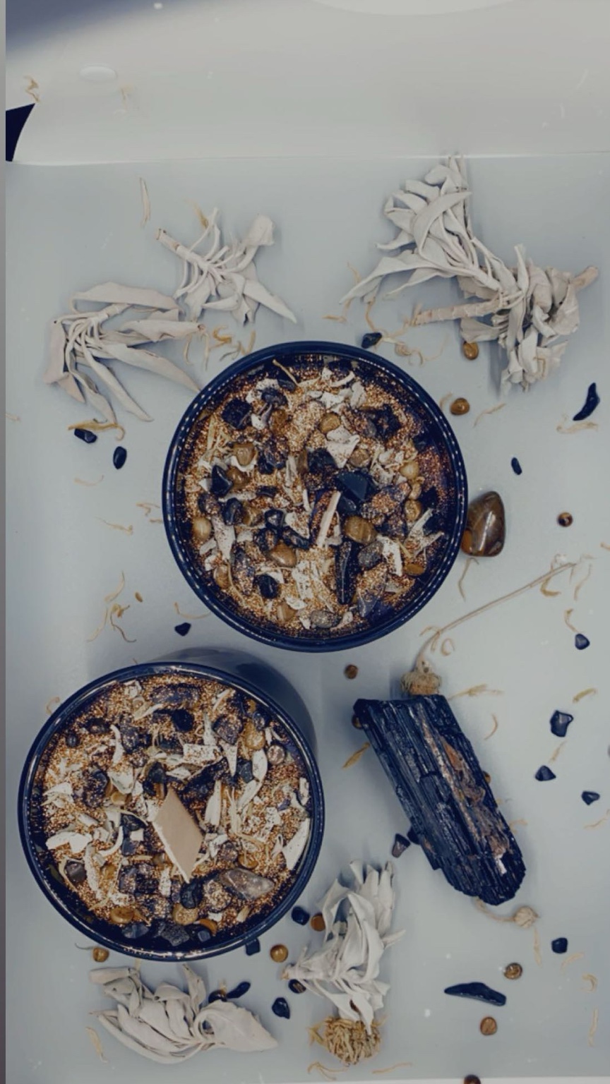 Two candles placed among sage bundles, stones, and dried florals.
